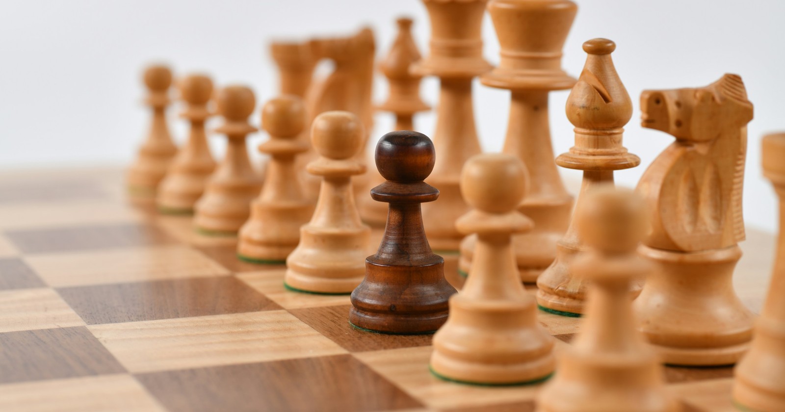 A single dark chess pawn standing in front of a row of light wooden chess pieces
